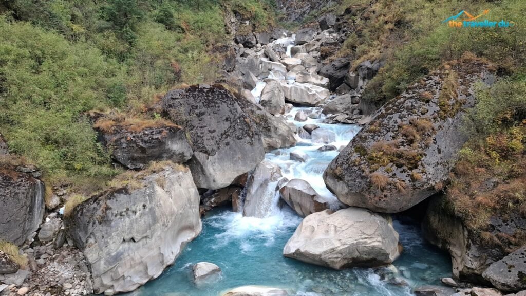 Turquoise glacier-fed stream flowing between boulders on the North Annapurna Base Camp trail