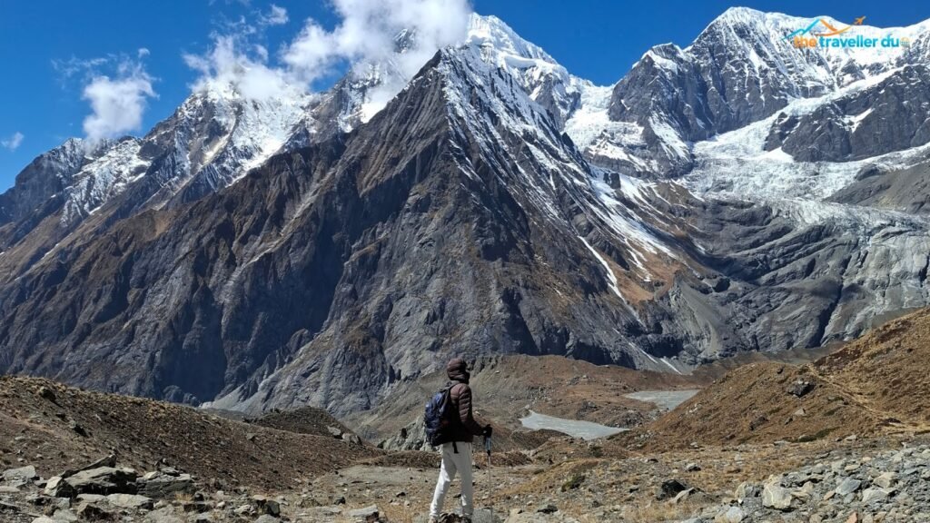 Trekker walking across the moraine toward North Annapurna Base Camp with snow peaks and glacial ponds